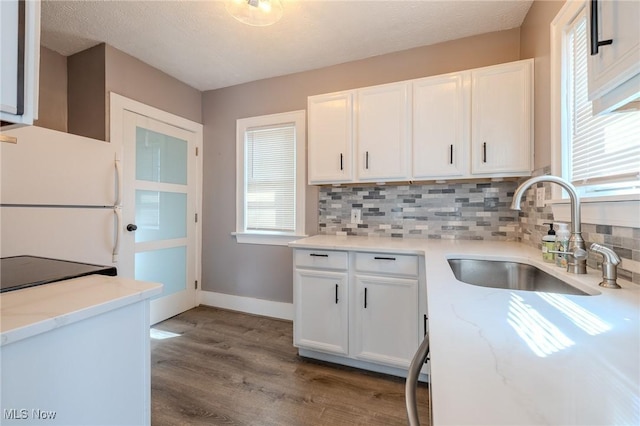 kitchen featuring a sink, tasteful backsplash, freestanding refrigerator, and white cabinetry