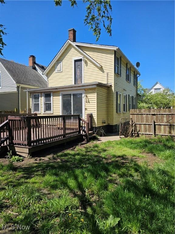 back of house with a lawn, a chimney, fence, and a deck