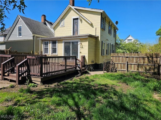 rear view of house featuring fence, a chimney, a lawn, and a deck