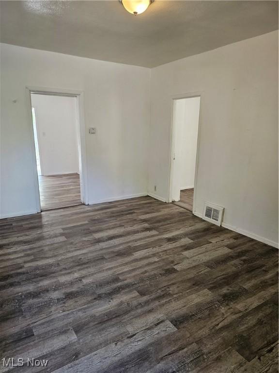 unfurnished room featuring visible vents, dark wood finished floors, and baseboards