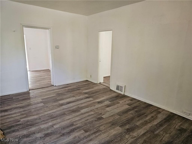 empty room featuring visible vents, baseboards, and dark wood-style floors