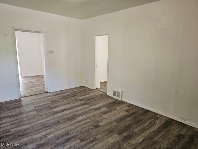 spare room with baseboards, dark wood-style floors, and visible vents