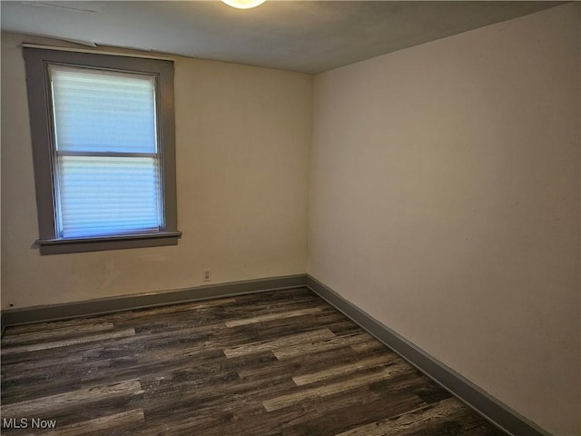 spare room featuring baseboards and dark wood-style floors