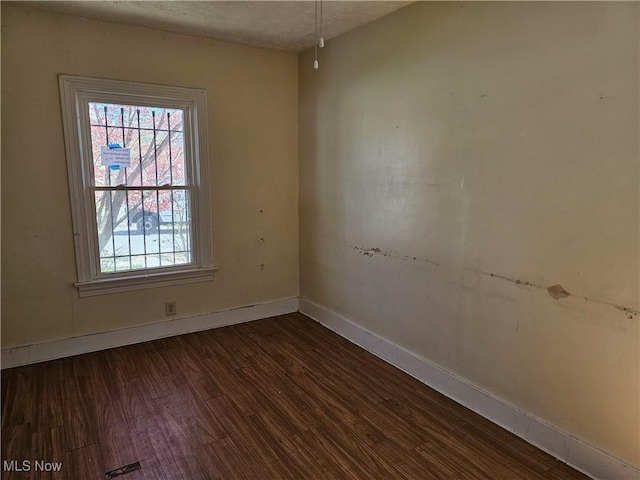 empty room with a textured ceiling, baseboards, and dark wood-style floors