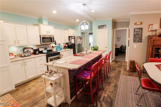 kitchen with a kitchen island with sink, crown molding, appliances with stainless steel finishes, dark wood finished floors, and a breakfast bar