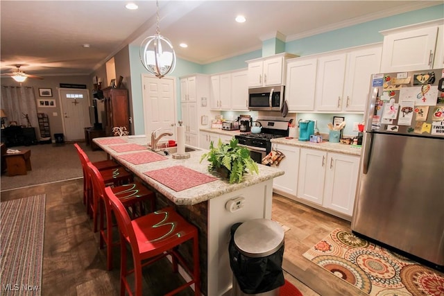 kitchen with crown molding, appliances with stainless steel finishes, a sink, white cabinets, and ceiling fan with notable chandelier