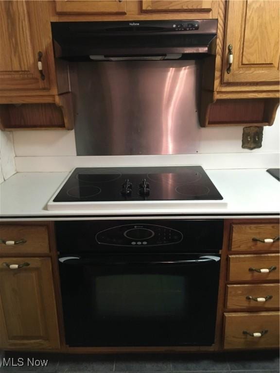 kitchen featuring light countertops, brown cabinets, under cabinet range hood, and black appliances