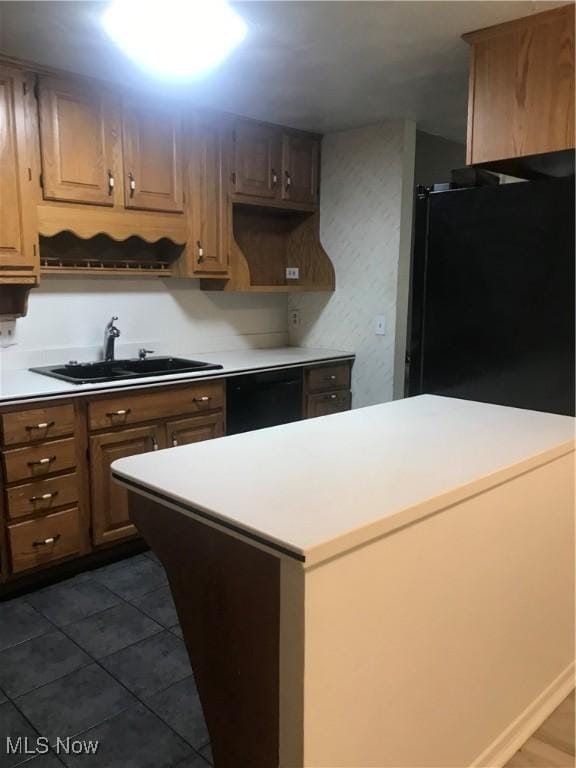 kitchen with a sink, light countertops, a kitchen island, dark tile patterned floors, and black appliances