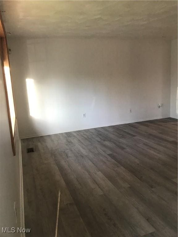 spare room featuring baseboards, dark wood finished floors, and visible vents