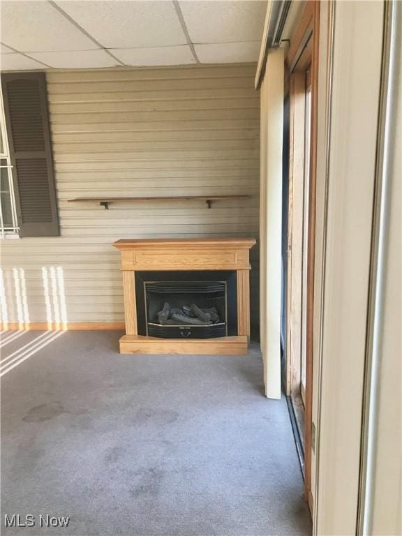 unfurnished living room featuring carpet floors, a paneled ceiling, wooden walls, and a fireplace