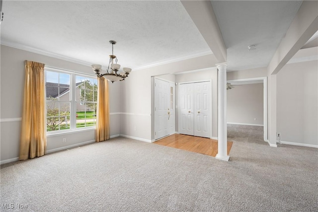 carpeted spare room with a notable chandelier, baseboards, ornate columns, visible vents, and ornamental molding