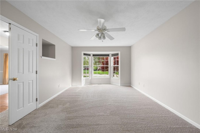 empty room with carpet floors, a textured ceiling, baseboards, and ceiling fan