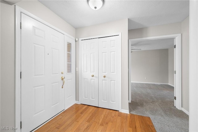foyer entrance with baseboards, a textured ceiling, and light wood-type flooring