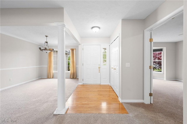 entryway featuring light colored carpet, baseboards, ornate columns, and a chandelier