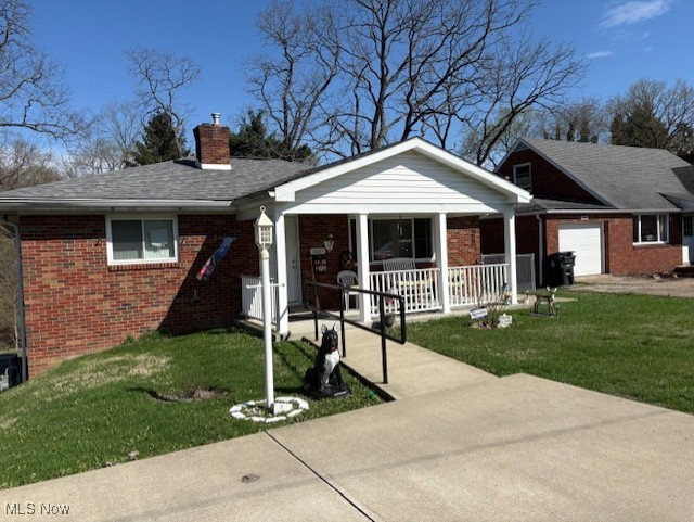 ranch-style home featuring a garage, a front lawn, covered porch, a chimney, and brick siding