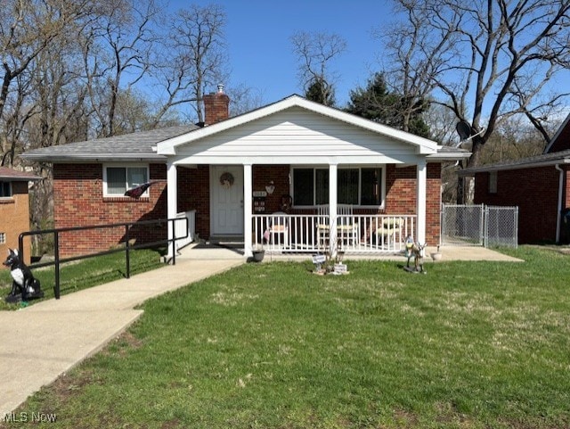 view of front of home featuring brick siding, a chimney, covered porch, and a front yard