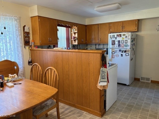 kitchen with freestanding refrigerator, brown cabinetry, and visible vents
