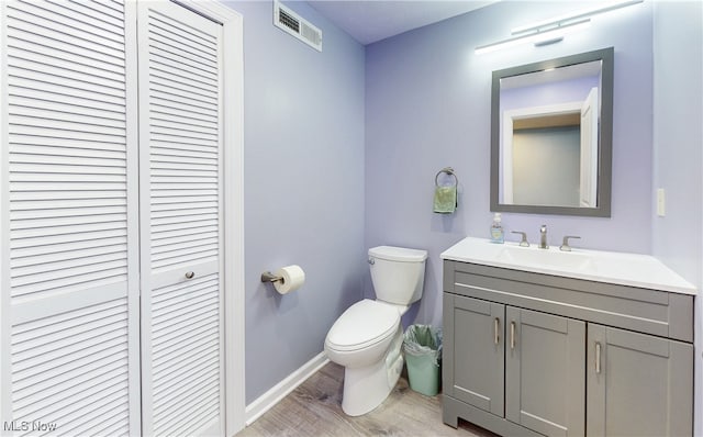 half bath with visible vents, a closet, vanity, wood finished floors, and toilet