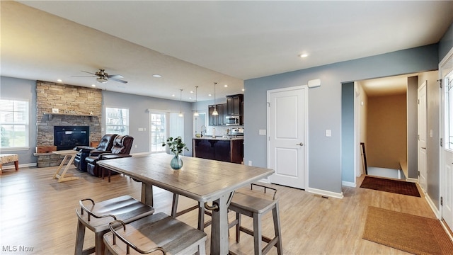 dining space featuring light wood-style floors, baseboards, a stone fireplace, ceiling fan, and recessed lighting