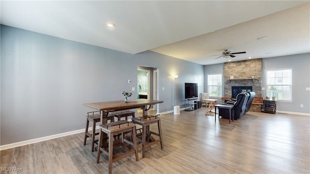 dining room featuring a fireplace, baseboards, ceiling fan, and light wood-type flooring