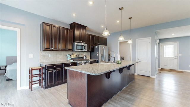 kitchen with light wood-style floors, baseboards, a kitchen breakfast bar, a sink, and appliances with stainless steel finishes