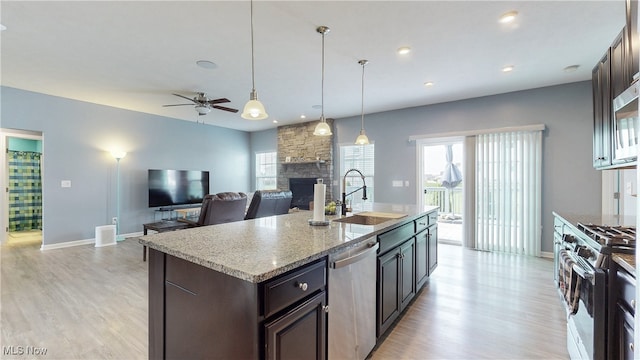 kitchen with dark brown cabinetry, a stone fireplace, a sink, light wood-style flooring, and appliances with stainless steel finishes