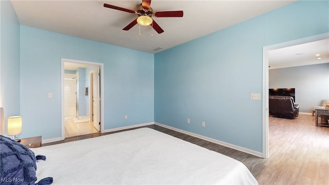 bedroom with baseboards, ceiling fan, ensuite bath, and wood finished floors