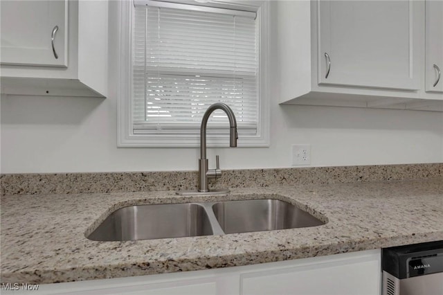 interior details with a sink, white cabinetry, dishwashing machine, and light stone countertops