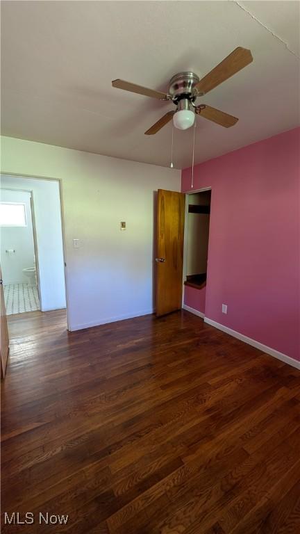 empty room featuring baseboards, a ceiling fan, and dark wood-style floors
