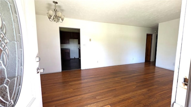 empty room featuring a textured ceiling, wood finished floors, and a chandelier