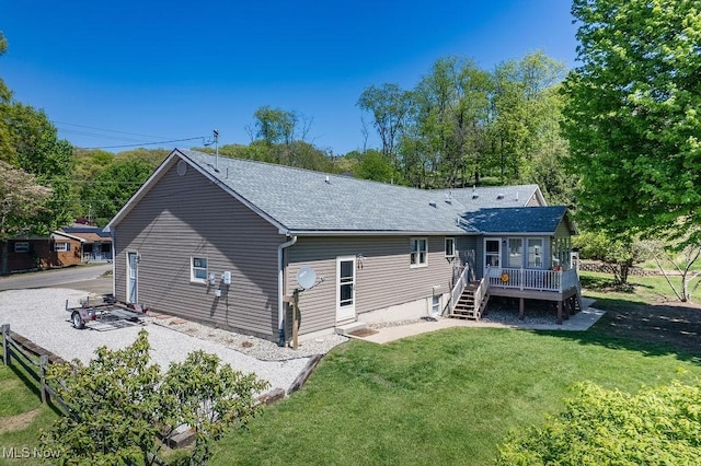 rear view of property with roof with shingles, a lawn, and a deck