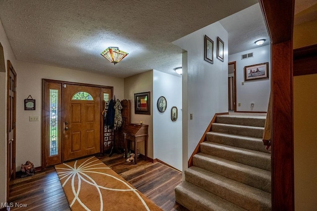 foyer entrance featuring a textured ceiling, baseboards, wood finished floors, visible vents, and stairway