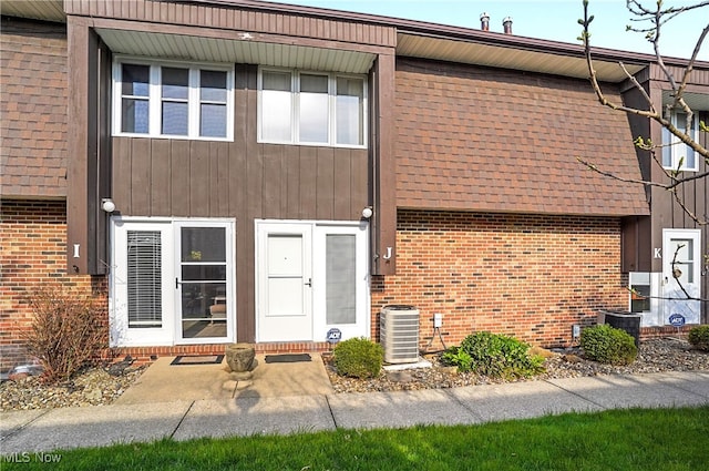view of front facade featuring central air condition unit, brick siding, and a shingled roof