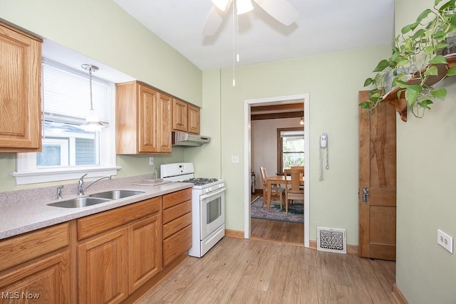 kitchen featuring a sink, light wood finished floors, gas range gas stove, under cabinet range hood, and visible vents