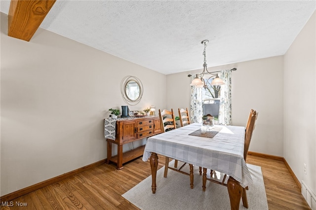 dining room featuring a textured ceiling, baseboards, visible vents, and light wood-type flooring
