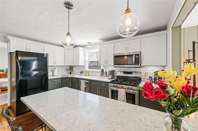 kitchen with white cabinets, decorative light fixtures, appliances with stainless steel finishes, and tasteful backsplash