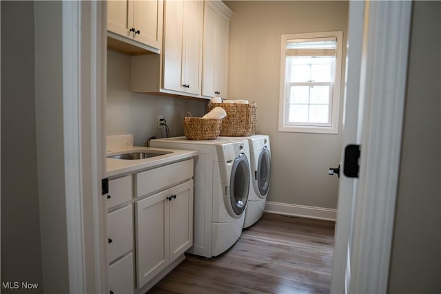 laundry room with cabinet space, a sink, separate washer and dryer, baseboards, and wood finished floors