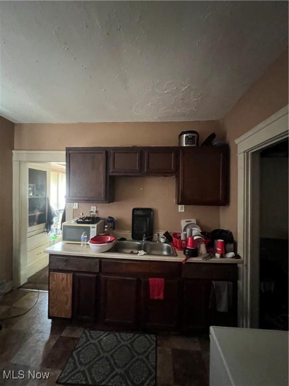 kitchen featuring light countertops, a sink, stone finish floor, and dark brown cabinets