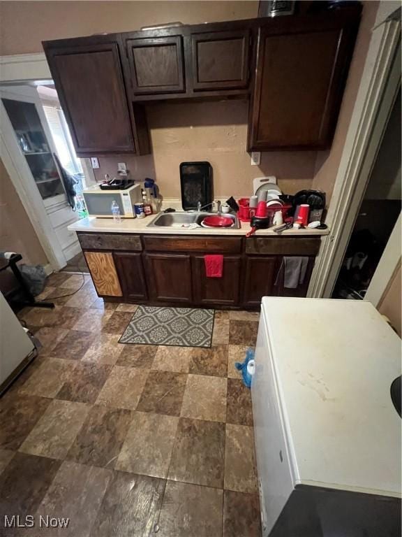 kitchen with light countertops, dark brown cabinetry, a sink, and stone finish floor