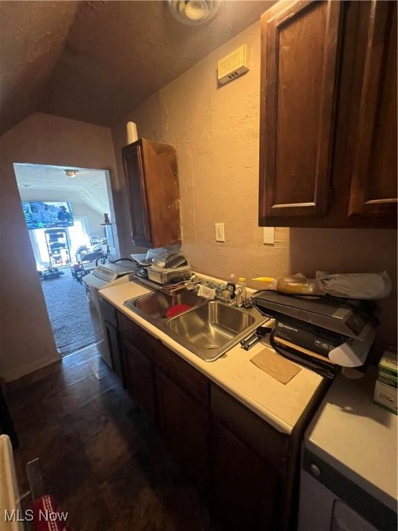 kitchen with a sink, light countertops, dark brown cabinetry, and lofted ceiling