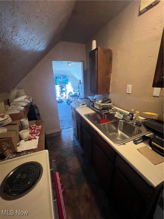 kitchen featuring stove, a sink, and lofted ceiling