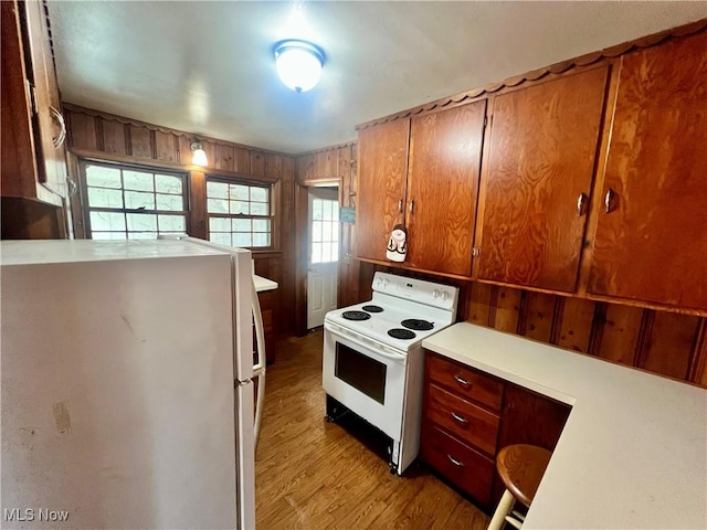 kitchen with wood finished floors, white appliances, wooden walls, light countertops, and brown cabinets