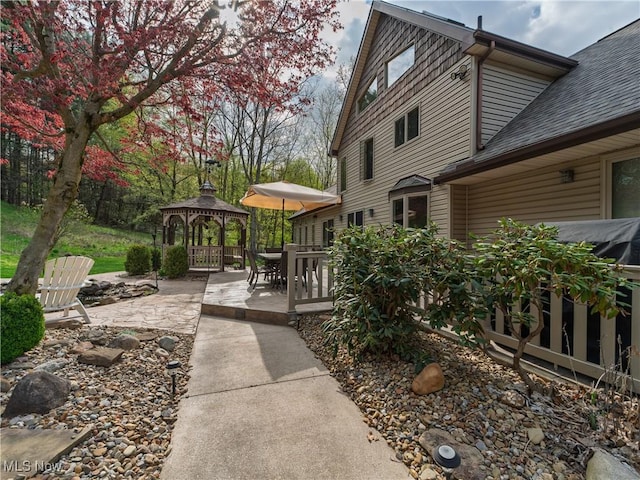 view of property exterior with roof with shingles, a patio, a gazebo, and outdoor dining space