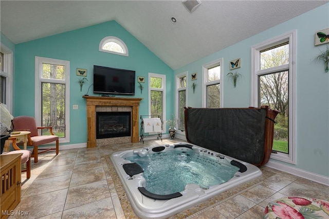 interior space featuring baseboards, vaulted ceiling, a tile fireplace, and a wealth of natural light