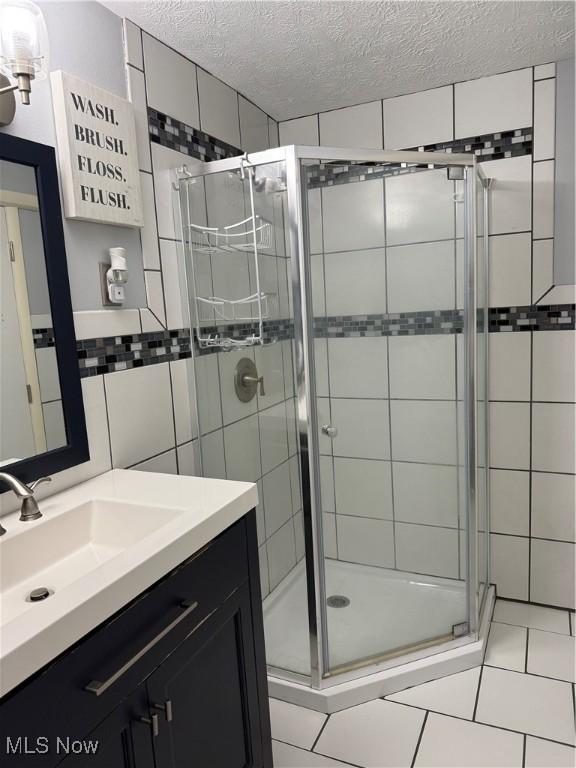 full bathroom featuring a textured ceiling, tile walls, a stall shower, vanity, and tile patterned floors