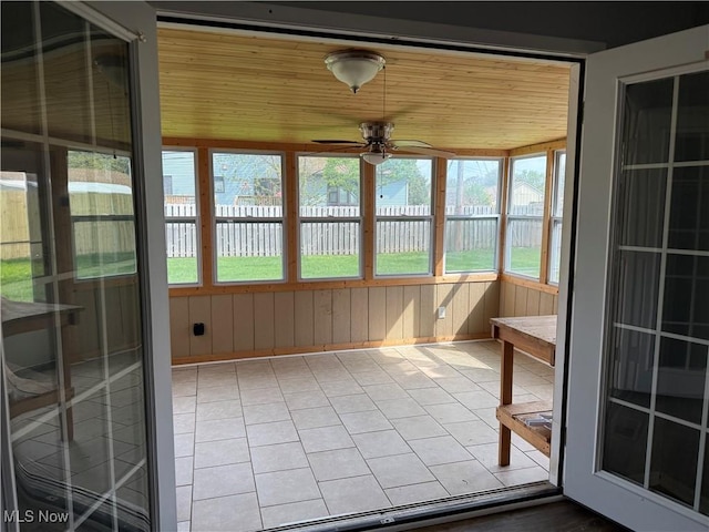 unfurnished sunroom with ceiling fan, wood walls, wooden ceiling, and tile patterned floors