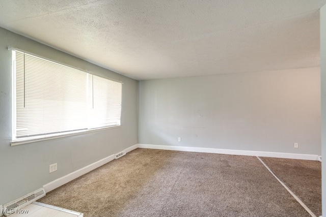 carpeted spare room with visible vents, a textured ceiling, and baseboards