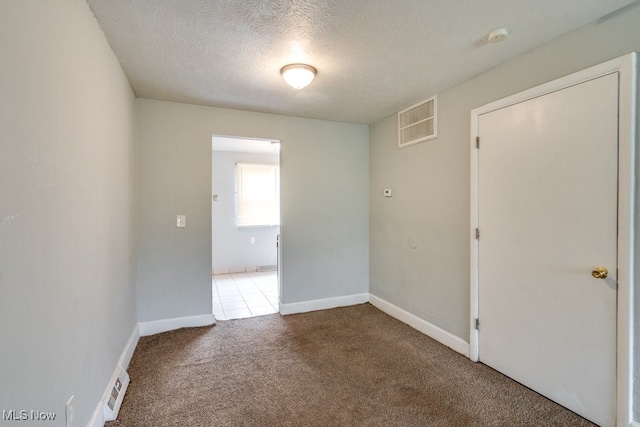 carpeted spare room featuring visible vents, a textured ceiling, and baseboards