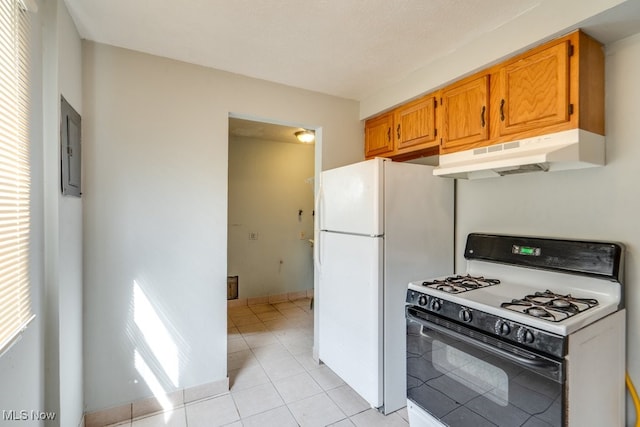 kitchen featuring range with gas stovetop, freestanding refrigerator, under cabinet range hood, brown cabinets, and light tile patterned floors