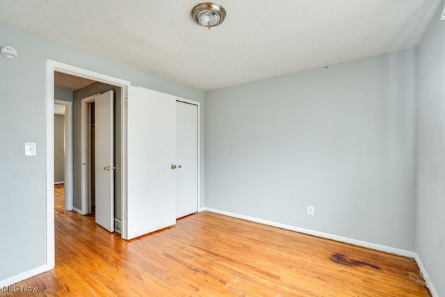 unfurnished bedroom featuring baseboards, light wood-style flooring, and a closet